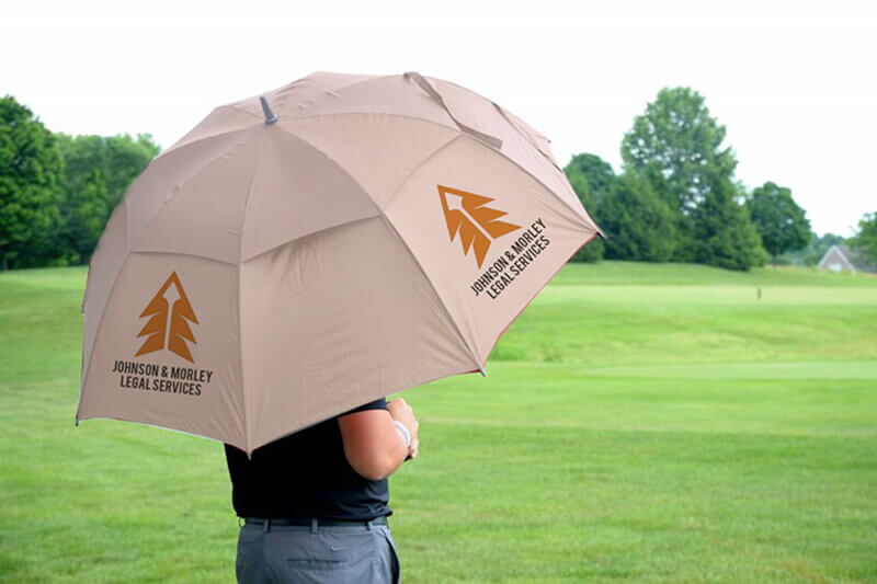 Man holding beige golf umbrella with custom printing while looking out over a golf course