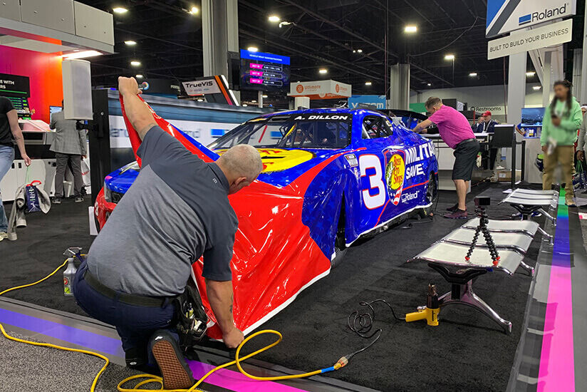 People wrapping a vehicle in a live vehicle wrapping demo at PRINTNG United