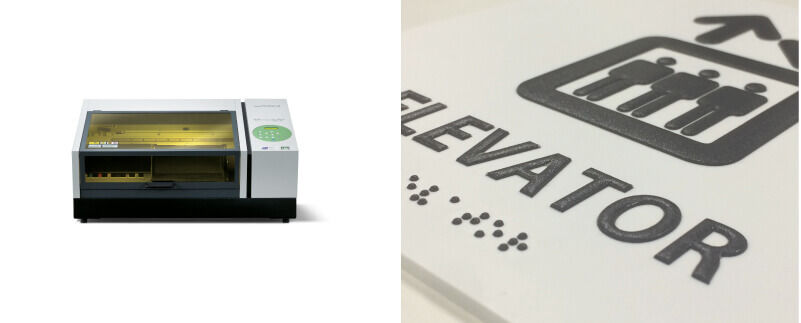 Roland DG LEF-12 desktop UV printer next to elevator sign with braille