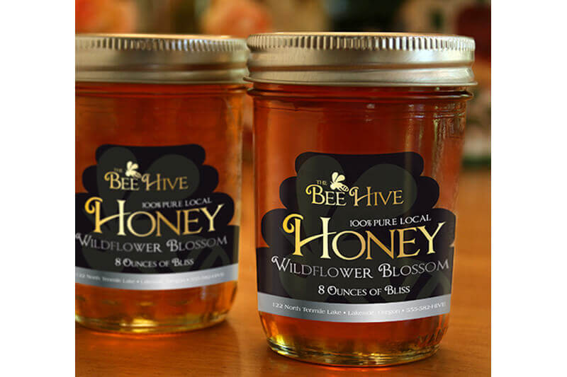 Dos frascos etiquetados “Bee Hive Honey” llenos de miel sobre una mesa.