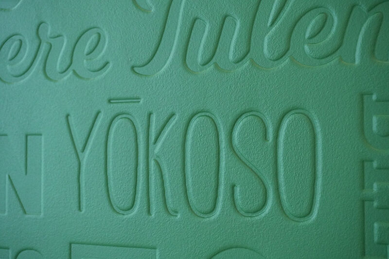 Green wallcovering embossed with the word "welcome" in many languages