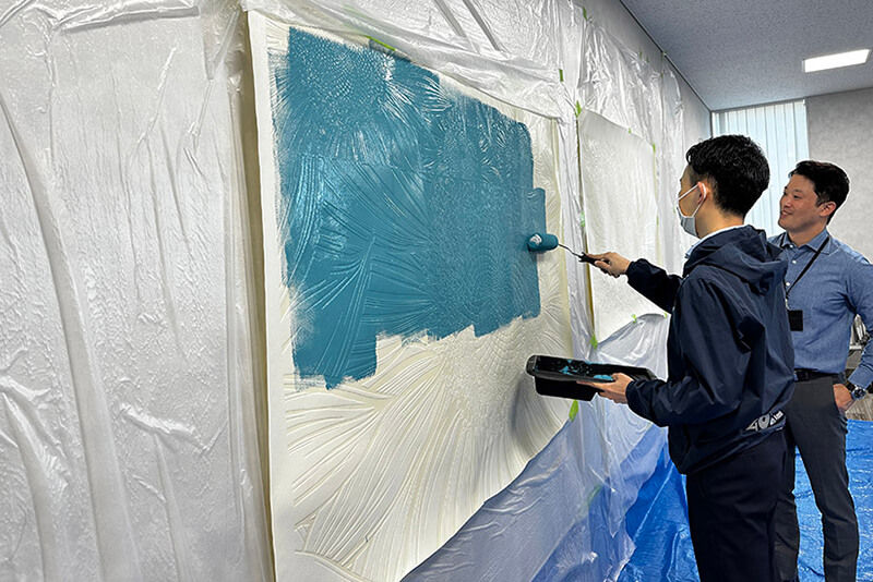 Dos hombres aplicando tintas a un gran gráfico de pared con superficies en relieve.
