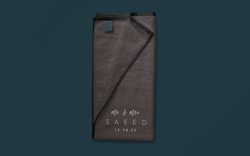Toalla gris para manos con impresión en blanco: “Mr. and Mrs. Saeed 12.14.23” (“Sr. y Sra. Saeed, 14 de diciembre del 2023”)