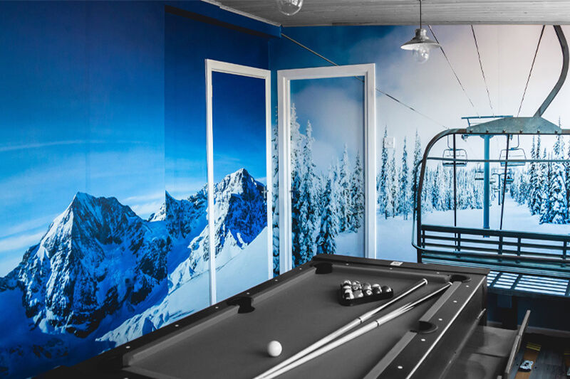 Mesa de billar en salón con gráficos de pared en blanco y azul mostrando un escenario de montaña y telesilla de esquiar.