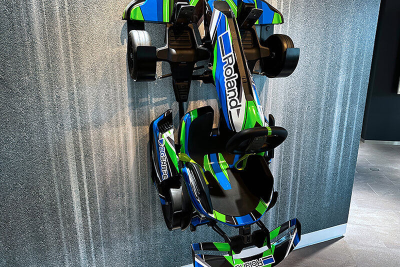 A go cart with vehicle graphics hung vertically on a wall in the Roland DG exhibition space