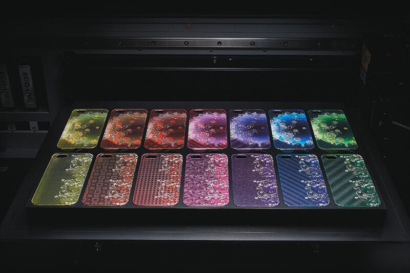 Roland DG benchtop UV printer open to show colorful prints on multiple phone cases.
