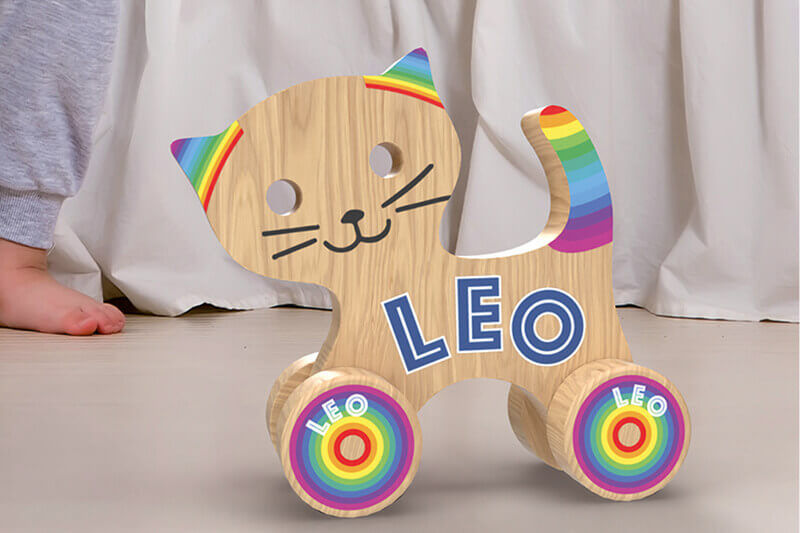 Gato de juguete de madera sobre ruedas con coloridos gráficos y el nombre “LEO”; en el medio