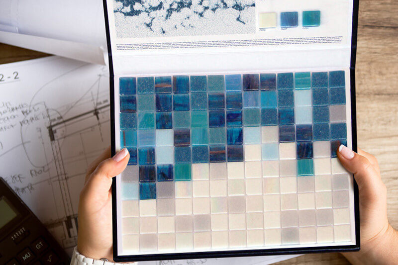 Hands holding sample mosaic tiles on UV-printed sample board.
