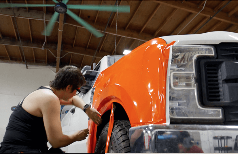 Hombre instalando una rotulación color naranja en un camión.