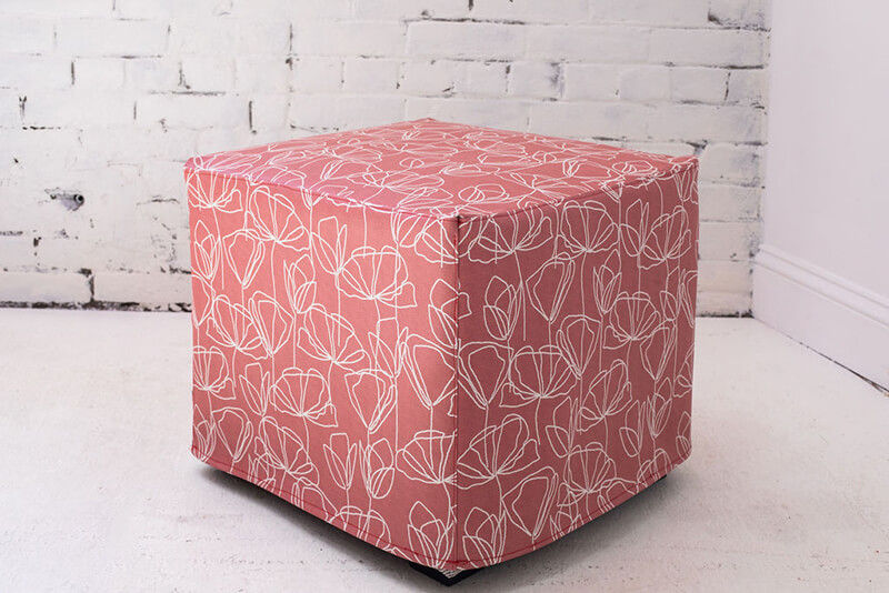 Ottoman covered with red and white printed textile in a white room.