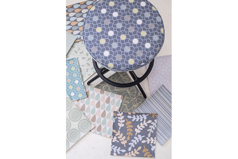 Top-down view of a stool with printed graphics on the seat, on the floor are pattern sample squares