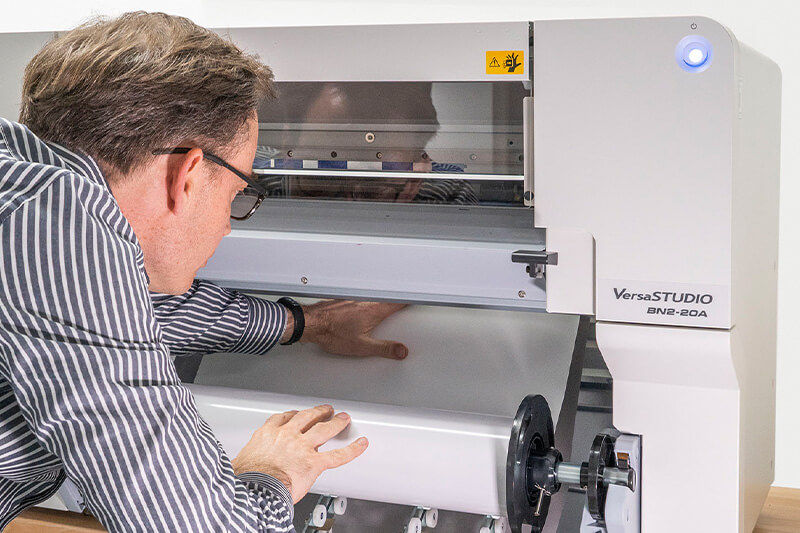 Person adjusting media in Roland DG VersaSTUDIO BN2-20.