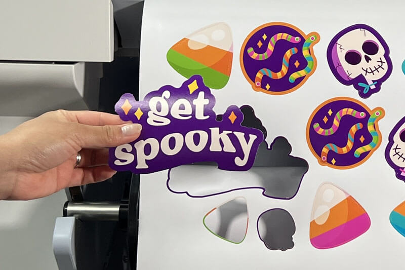 Hand showing graphics "get spooky" in front of printed sheet of Halloween designs.