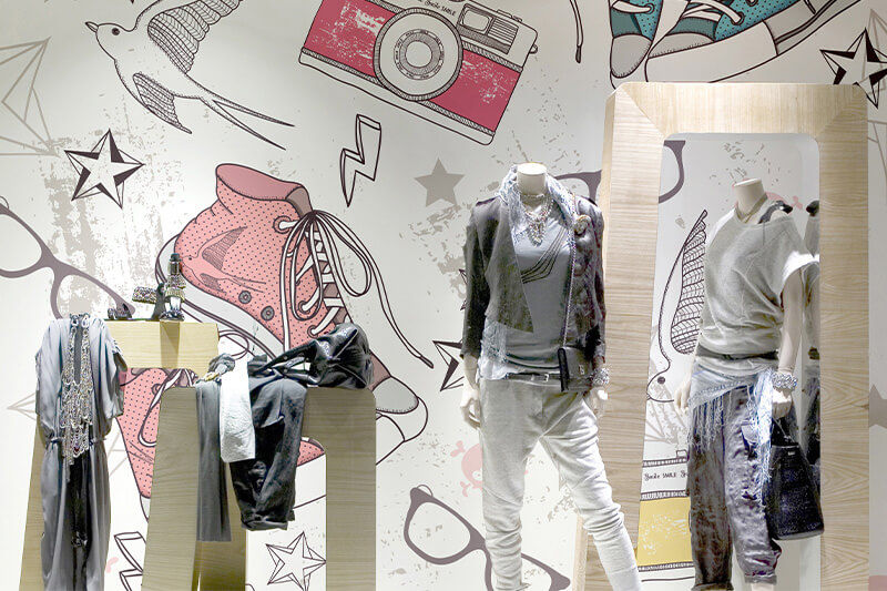 Clothed mannequins in front of a retail wall wrapped in colorful graphics.