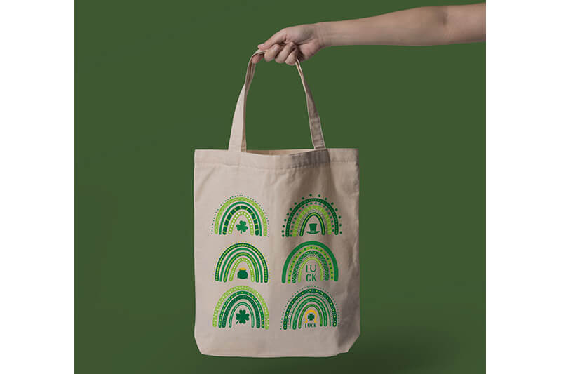 Hand holding a tote bag with six St. Patrick's Day-themed designs.