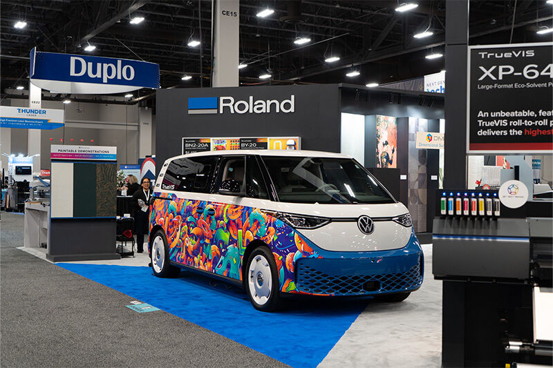 Un bus eléctrico VW rotulado con gráficos de vehículos en el pabellón Roland DGA de la feria comercial ISA.