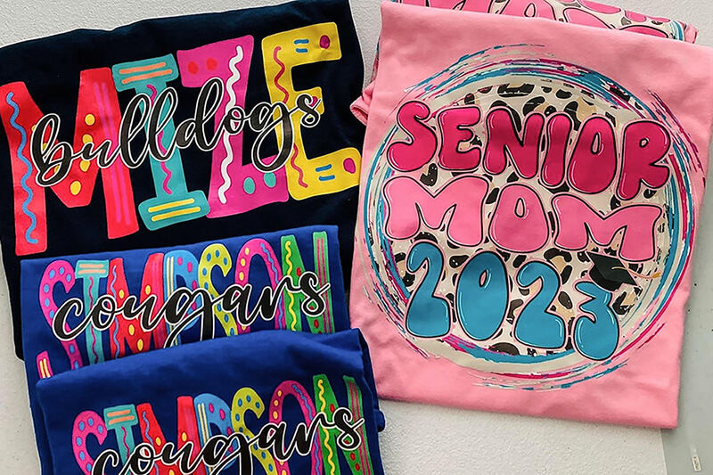 Coloridos gráficos en camisetas dobladas, impresos usando impresoras VersaSTUDIO® de Roland DG