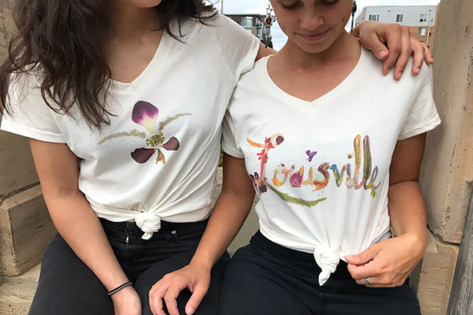 Two people in t-shirts printed with colorful designs using a Roland DG BT-12 direct-to-garment printer.