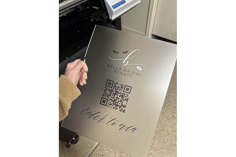 Hand holding clear acrylic sign with silver lettering saying "Enter to Win" and QR code from Bella Bridal Beauty.