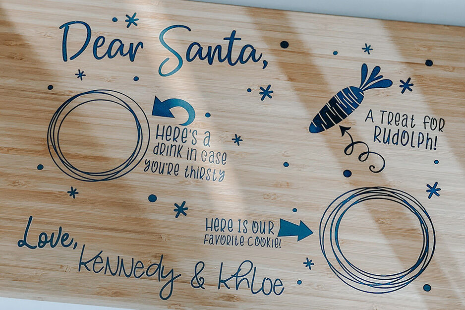 Small beige sign with blue writing and graphics that says "Dear Santa" with gift ideas described, "Love, Kennedy & Khloe"