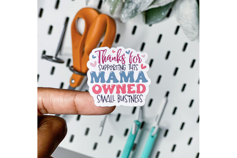 Finger holding sticker that says "Thank you for supporting a mama owned small business"