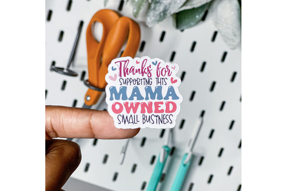 Finger holding sticker that says "Thank you for supporting a mama owned small business"