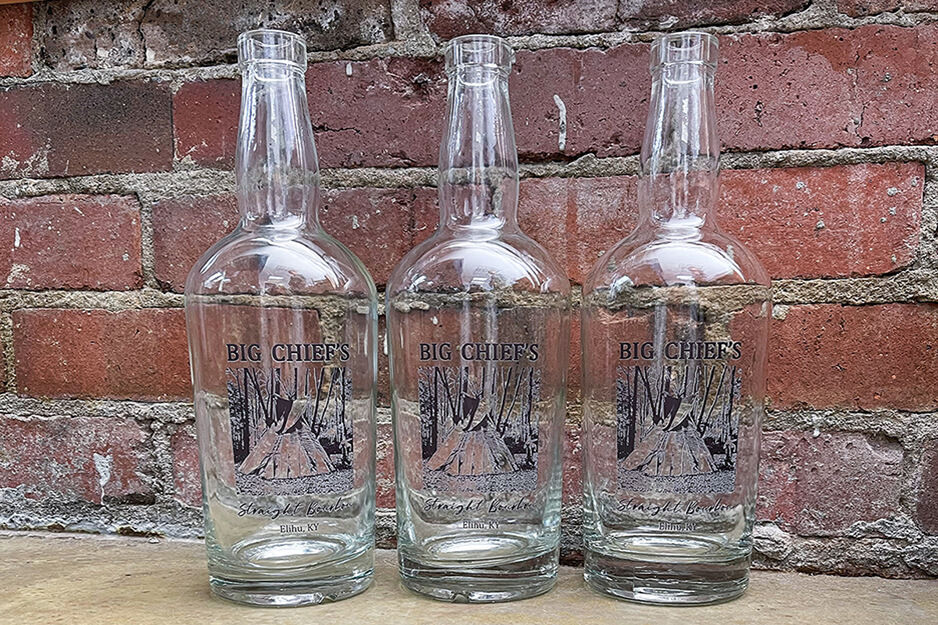 Three clear bottles with blue lettering on a wooden surface with a red brick background