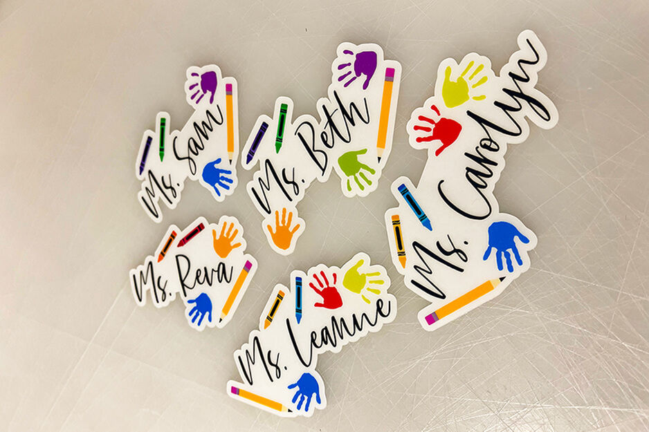 Cinco coloridas calcomanías recortables con nombres de maestros y gráficos escolares, incluyendo manos y lápices.