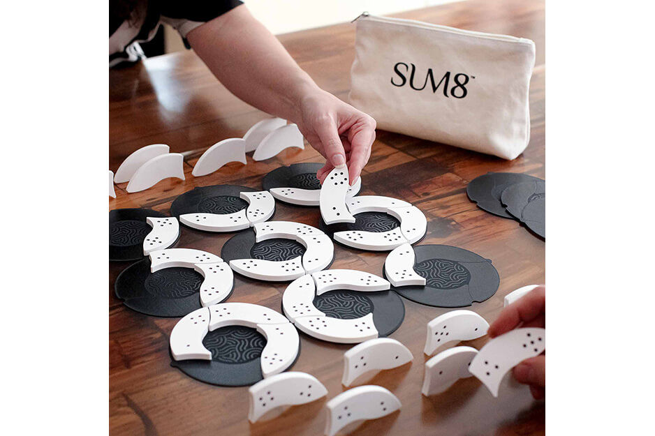 Hand placing curved playing pieces of game "Sum8" on board.