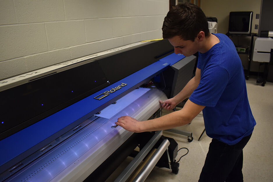 A student at Roseville's student-run print shop adjusts media on the Roland TrueVIS VG2 digital printer/cutter