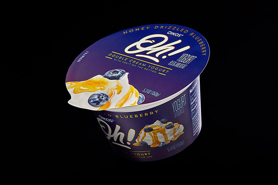 Individual serving cup angled so "Oh" brand packaging on the top and front of container are visible, showing white lettering on deep blue background.