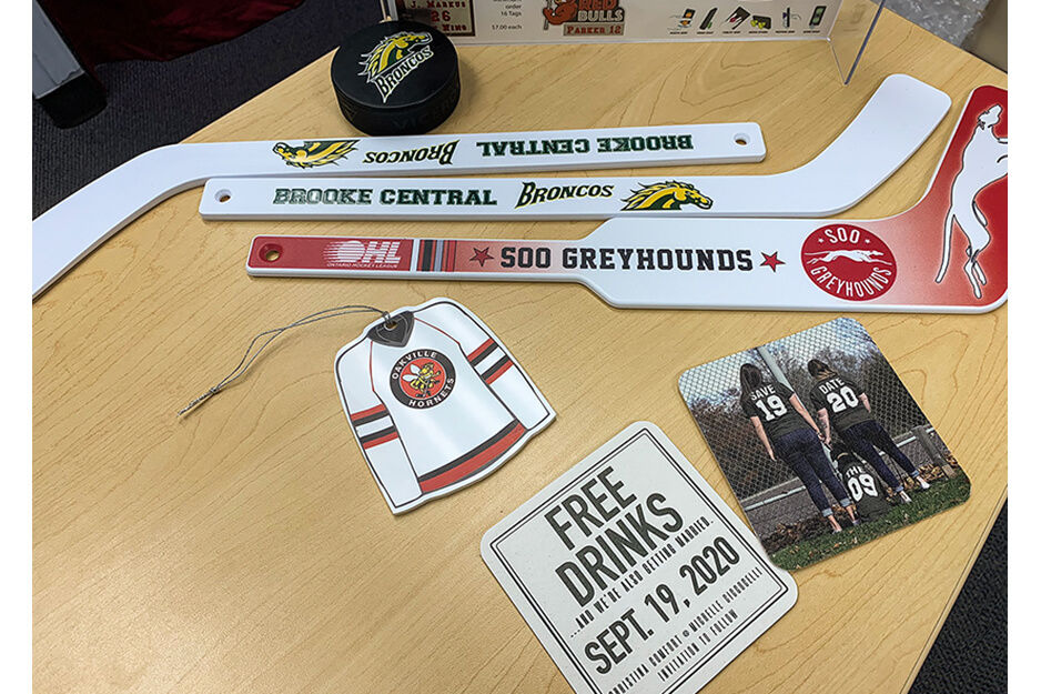 Examples of UV-printed products including small hockey sticks, pucks, tags, coasters, and signs