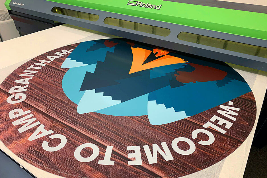 A sign for Camp Grantham emerges from Advanced Sign's Roland DG VersaUV flatbed printer.