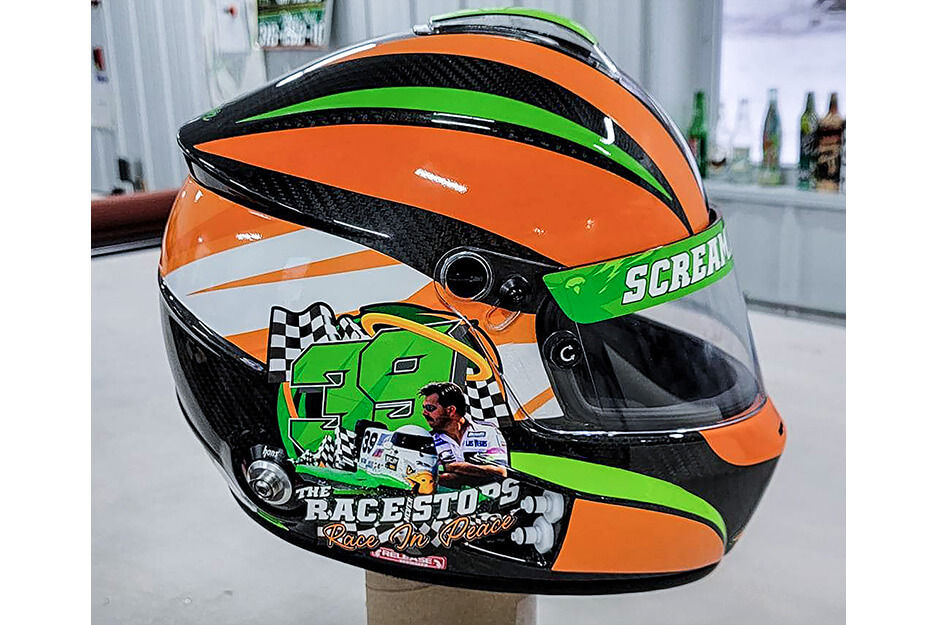 Racing helmet with orange, green, black and white graphics.