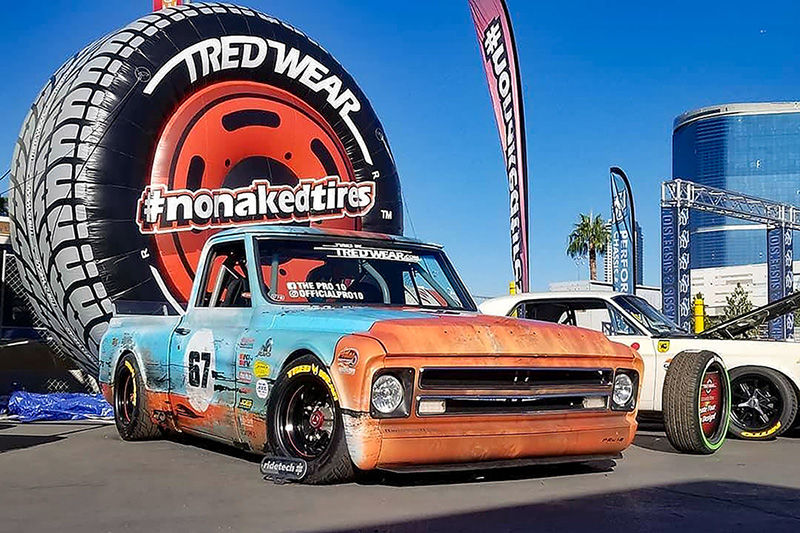 Vehículo rotulado en gráficos naranja y azules frente a un neumático gigante Tred Wear