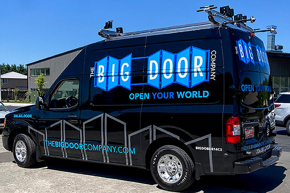Furgoneta de paneles negros rotulados con gráficos promocionando The Big Door Company