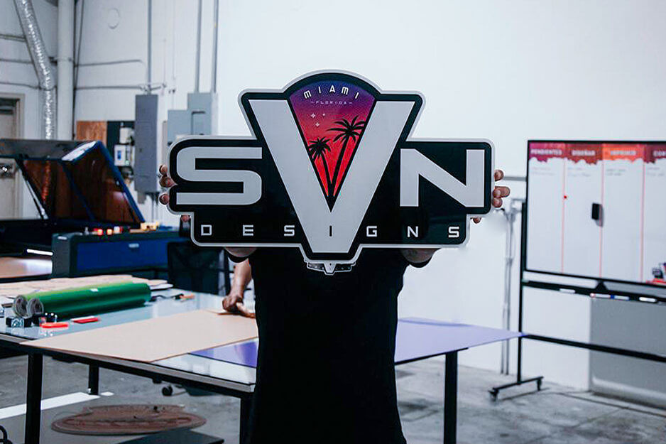 Man holds SVN Designs logo sign in front of his face.