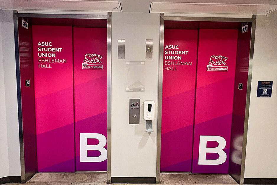 Dos puertas de elevador rotuladas en gráficos rojos y rosados impresos con una impresora de tintas de resina AP-640.