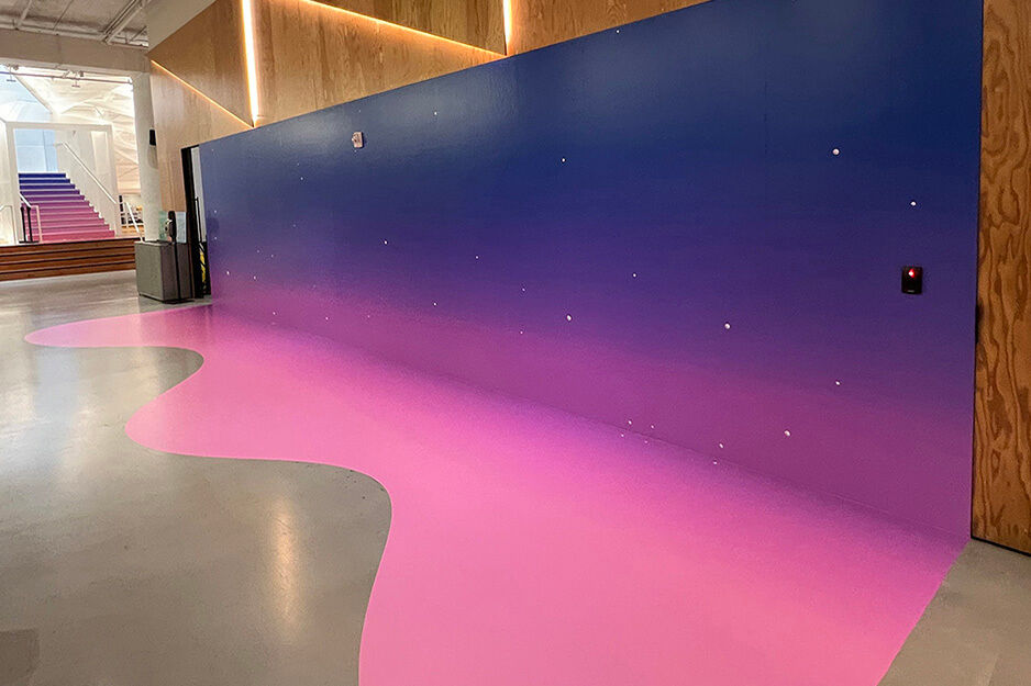 Pink to indigo graphics covering a wall and continuing onto the floor in curving pattern.