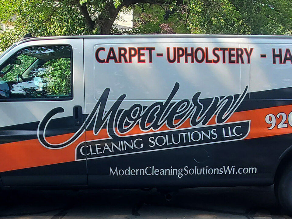 Side image of a cleaning service van with white, orange and black vehicle graphics.